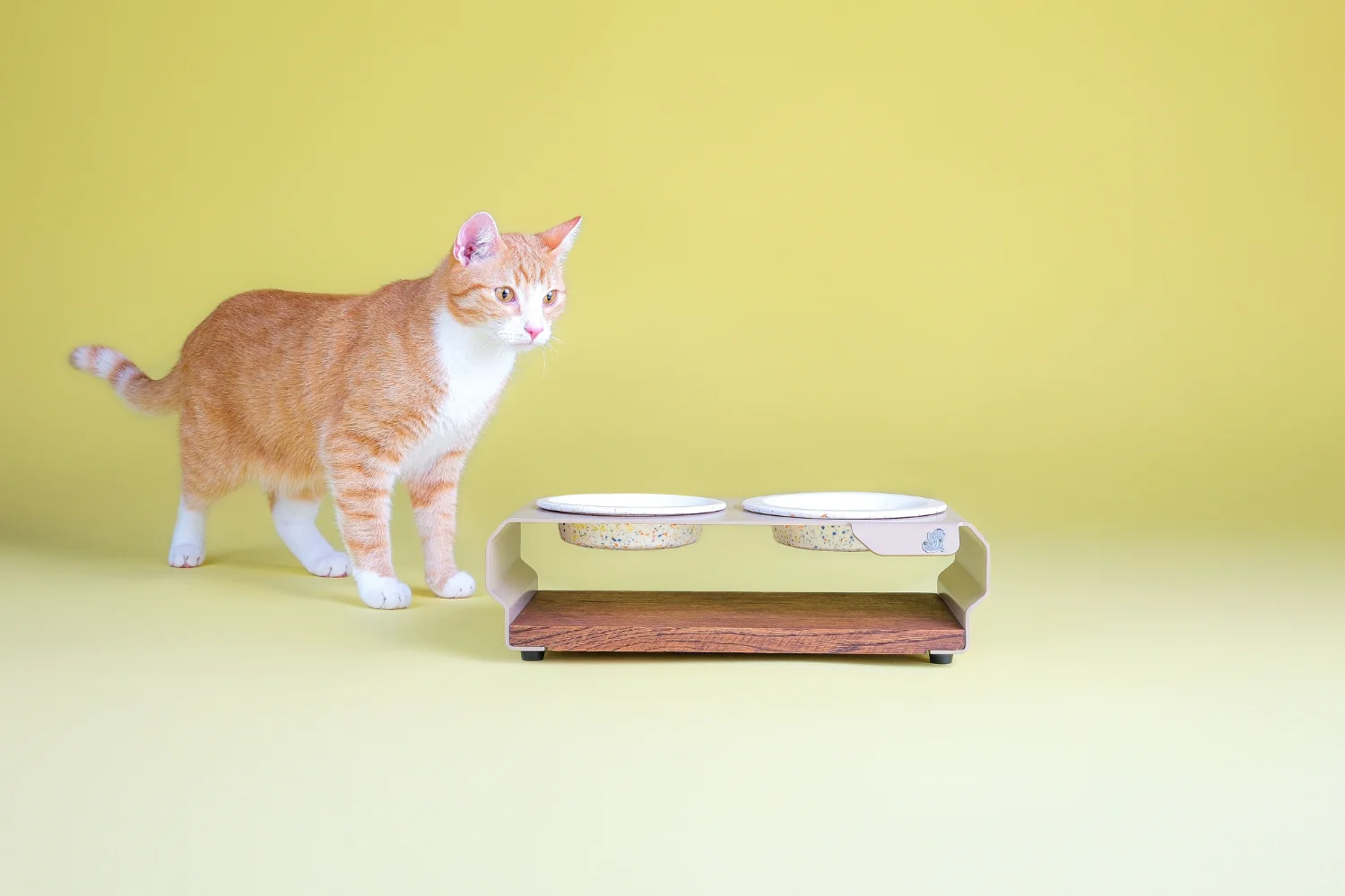 Orange-weisse-Katze-neben-einer-TierischEdel-Futterstation-mit-zwei-handgefertigten-Keramiknaepfen-im-Sprenkelmuster